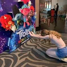 a woman kneeling down in front of a sign that says troll world on it with cartoon characters