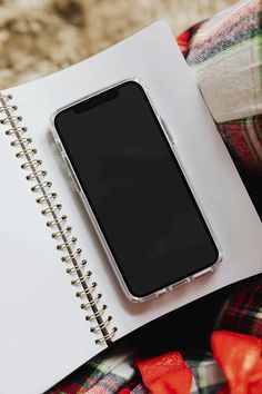 an open notebook sitting on top of a bed next to a cell phone and pen