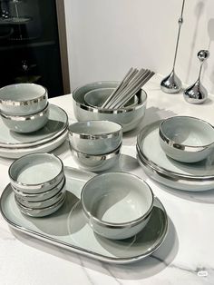 a white table topped with lots of silver plates and bowls next to utensils