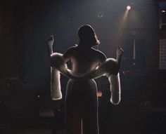 a woman standing in front of a stage with her arms up to the side, wearing fur gloves