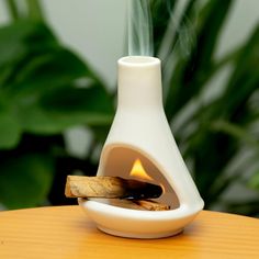 a white vase sitting on top of a wooden table next to a burning piece of wood