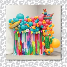 an assortment of balloons and streamers are on display in a white walled room with a cactus