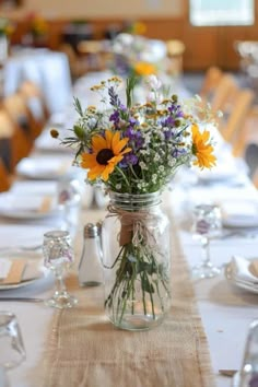 a mason jar filled with flowers sitting on top of a table covered in white linen