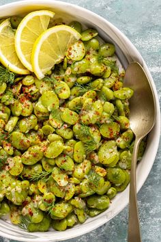 a white bowl filled with brussel sprouts and lemon wedges next to a spoon