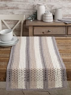 a wooden table topped with a white plate covered in a crochet blanket next to a cup and saucer