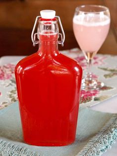 a red bottle sitting on top of a table next to a glass filled with liquid