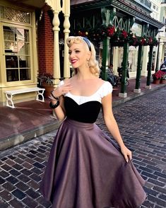 a woman in a purple and black dress is posing for the camera on a brick street