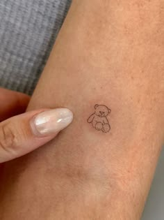 a small teddy bear tattoo on the wrist