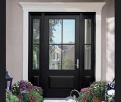 a black front door with flowers and potted plants in the foreground next to it