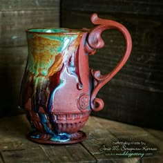 a red and green ceramic mug sitting on top of a wooden table next to a wall