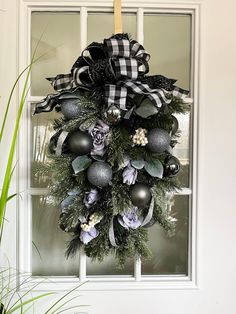 a wreath hanging on the front door with black and white decorations, greenery and balls