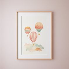 three hot air balloons floating in the sky on a pink wall with clouds below them