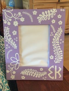 a purple frame with white flowers and leaves painted on the front is sitting on a table