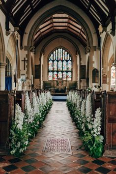 the aisle is lined with white flowers and greenery in front of a stained glass window