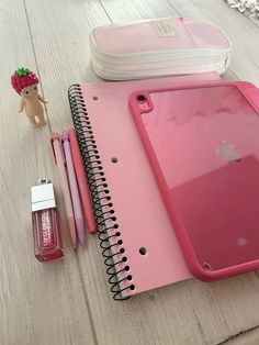 an open pink notebook sitting on top of a wooden table next to a small doll