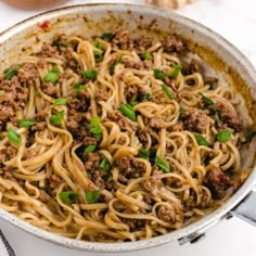 a skillet filled with noodles and ground meat on a white table next to garlic