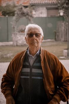 an old man with glasses standing in front of a building