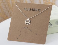 a card with a necklace on it sitting next to a box that says aquarius