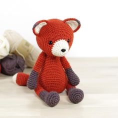 a knitted red fox sitting next to two balls of yarn