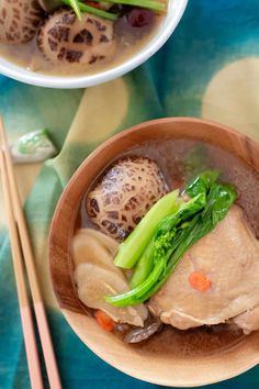 two bowls filled with meat and vegetables next to chopsticks on a blue table cloth