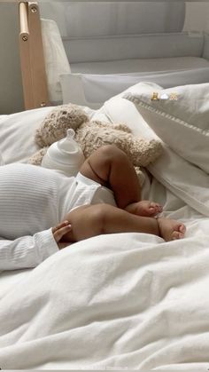 a baby laying in bed next to a teddy bear