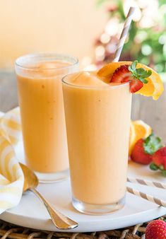 two glasses of smoothie with strawberries and oranges in the background on a wicker tray