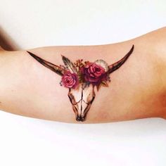 a woman's arm with a cow skull and roses tattoo on the left side