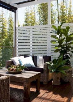 an outdoor living room with wooden floors and white privacy screens on the wall behind it