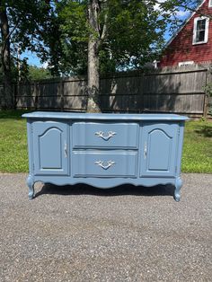 a blue dresser sitting in the middle of a driveway next to a tree and fence