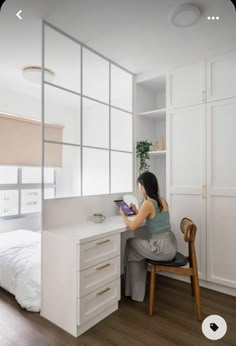 a woman sitting at a white desk in front of a bed with drawers on both sides