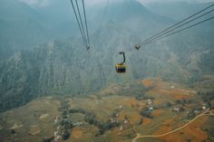 two people ride on a cable car above the valley and mountains in the foggy day