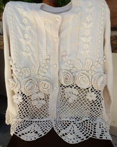 a white cardigan with lace and flowers on the front, sitting on a table