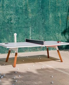 a ping pong table in front of a green wall with balls on the ground