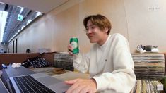 a man sitting in front of a laptop computer holding a can of beer and looking at the screen