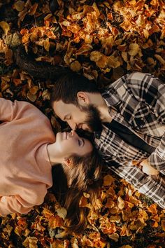 a man and woman laying on the ground covered in autumn leaves looking into each other's eyes