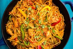 a skillet filled with noodles, meat and veggies on a blue table