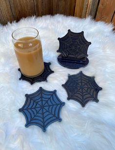 four coasters with spider web designs and a glass of orange juice on a white fur surface