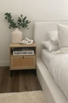 a white bed sitting next to a nightstand with a plant on top of it in a bedroom