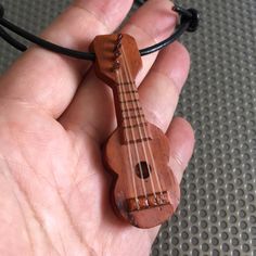 a hand holding a small wooden ukulele on a string