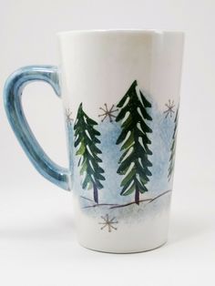 a blue and white coffee cup with trees painted on the side, sitting in front of a white background