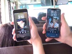 two people holding up their cell phones in the back of a bus while they are sitting down