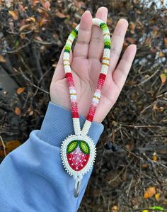 a hand holding a beaded necklace with an apple on it