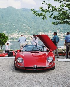 a red sports car with its hood open and people standing around looking at the cars