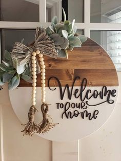 a welcome sign hanging on the side of a door with wood beads and greenery