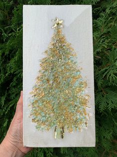 someone holding up a christmas tree made out of gold and green glitters on a white canvas