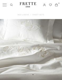 the bed linens and sheets are all white with gold embroidery on each pillowcase