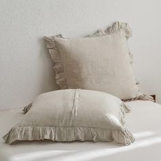 two pillows sitting on top of a bed with white sheets and ruffled trims