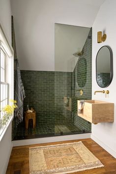 a bathroom with green tile and wooden flooring next to a mirror on the wall