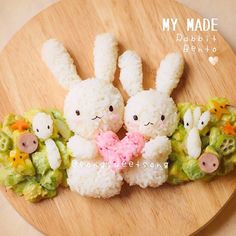 two small stuffed animals sitting on top of a wooden plate next to broccoli