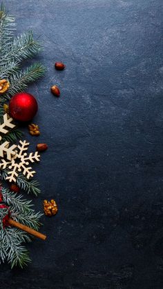 an arrangement of christmas decorations on a black surface with pine cones, cinnamon sticks and nuts